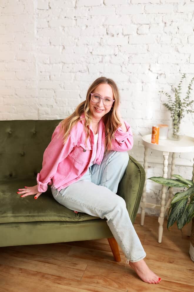 Chelsea Harold wearing a pink jacket and sitting on a green sofa