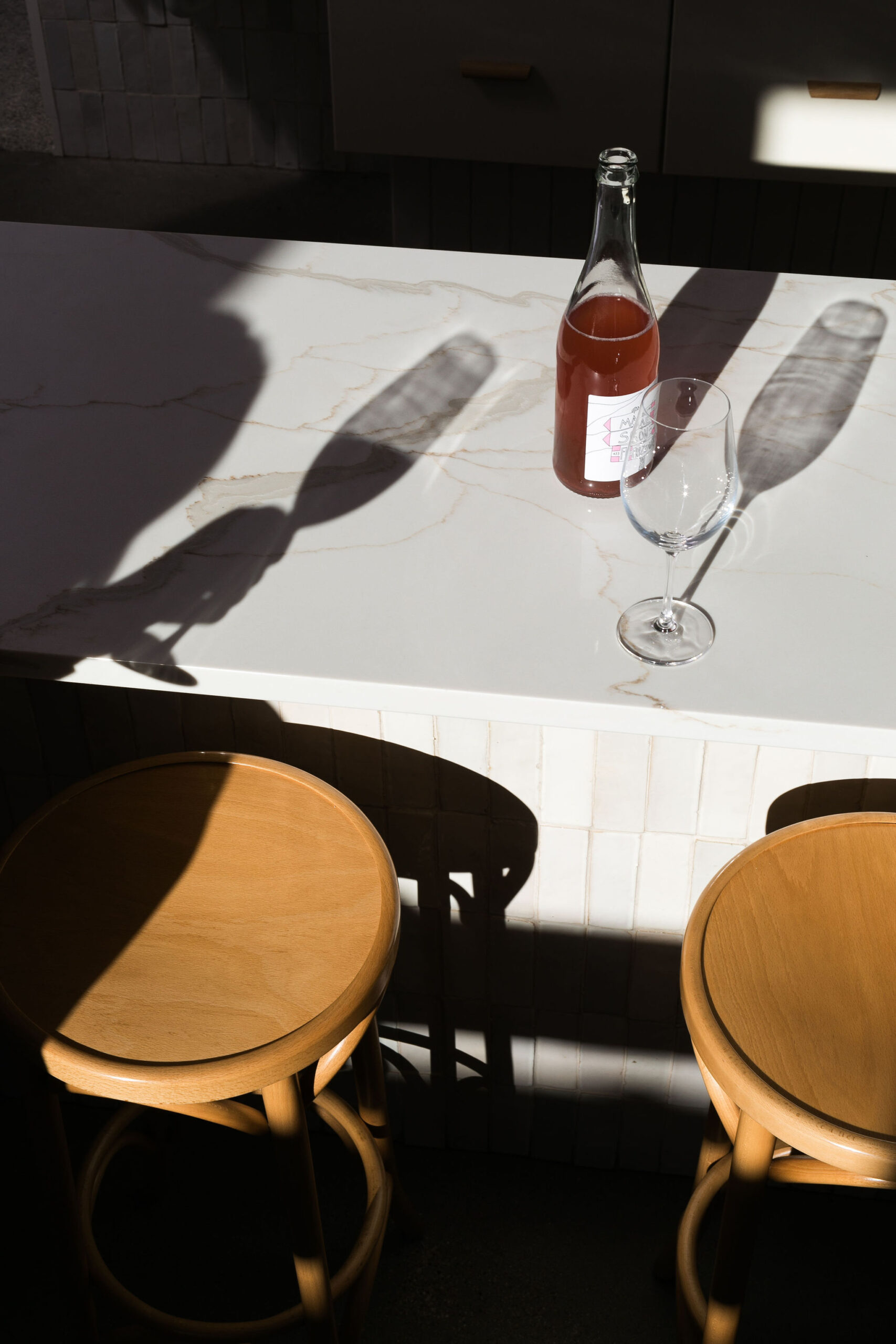 A picture of a wine bottle on a marble countertop with a shadow of someone holding a wine glass