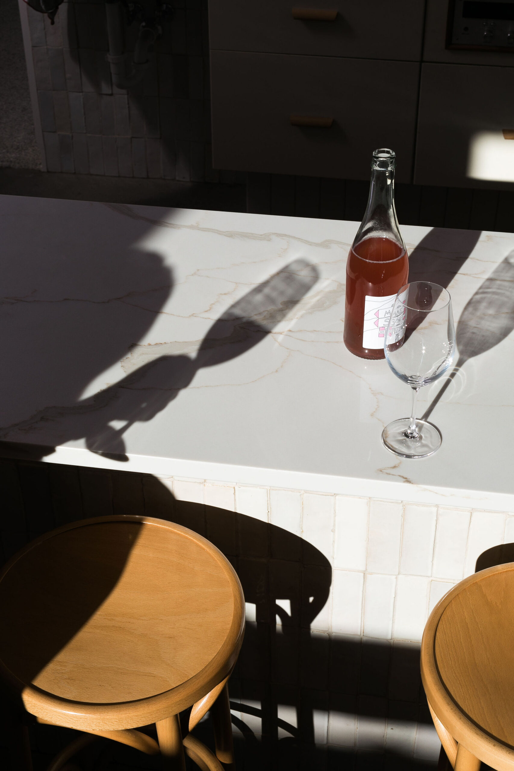 A wine glass and wine bottle on a counter and a shadow of someone holding a wine glass