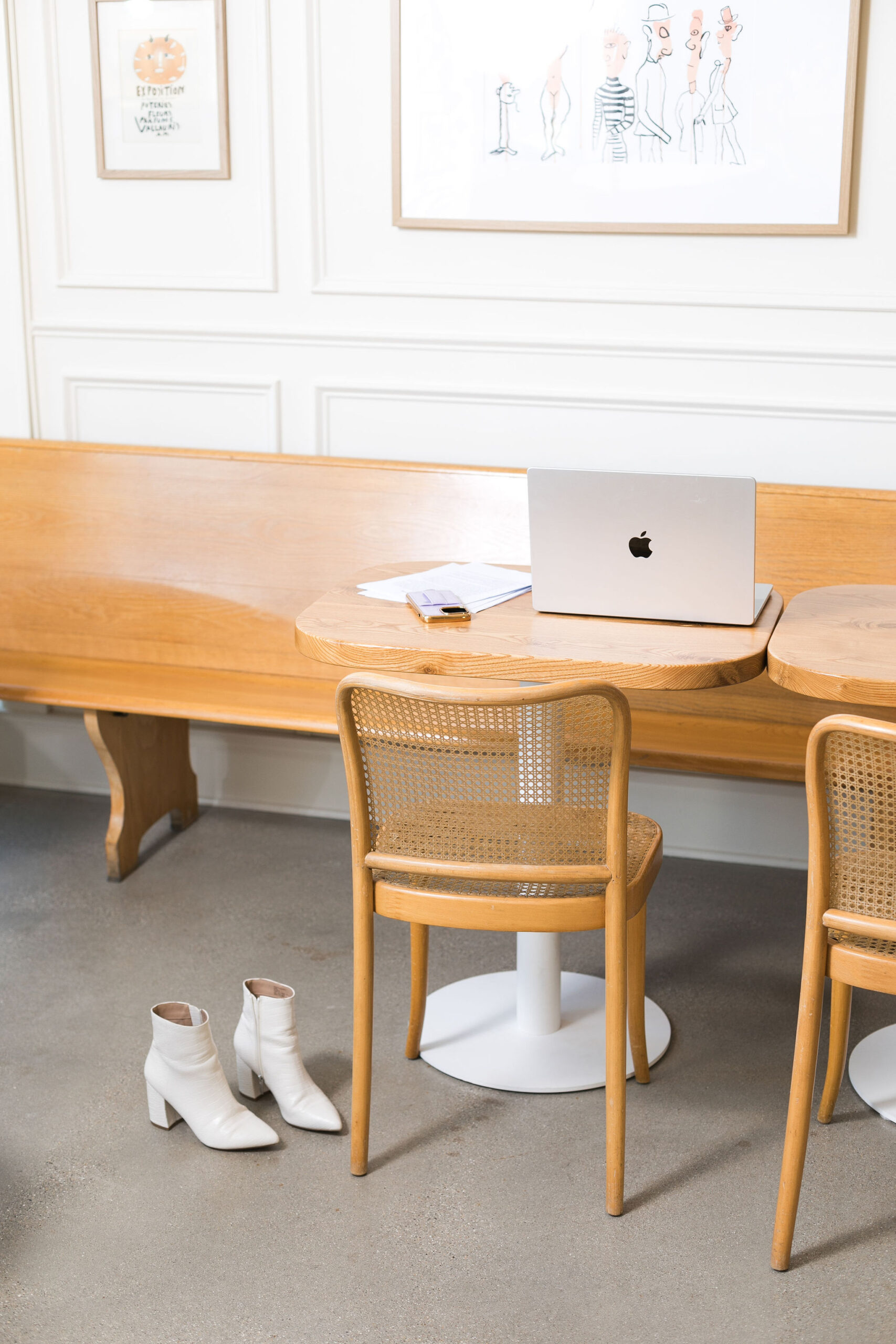 A desk with a laptop, 2 chairs, and a pair of white boots on the floor