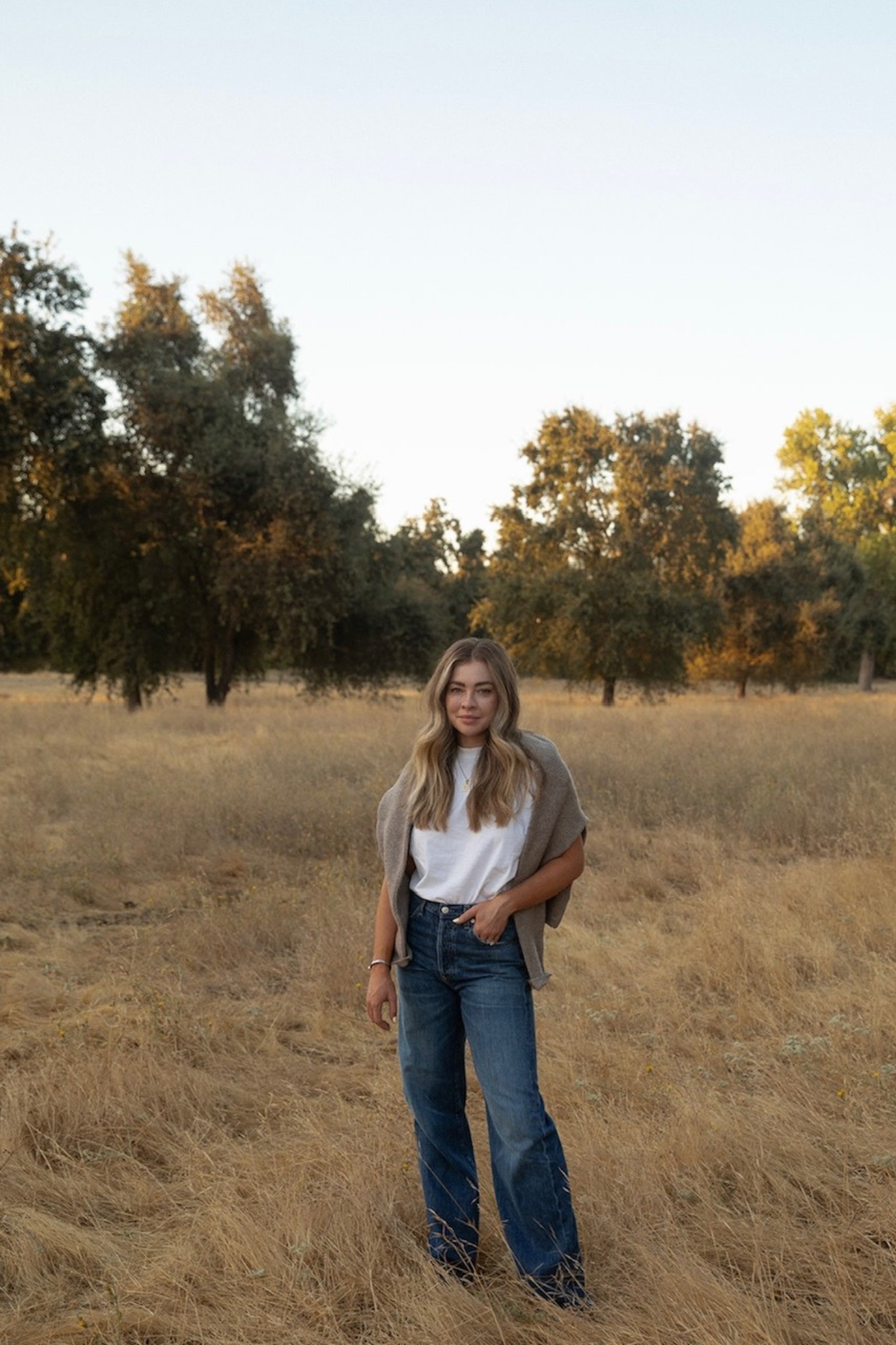 Photo of BryAnn standing on a field dressed in casual clothing (jeans, white t shirt, cardigan)