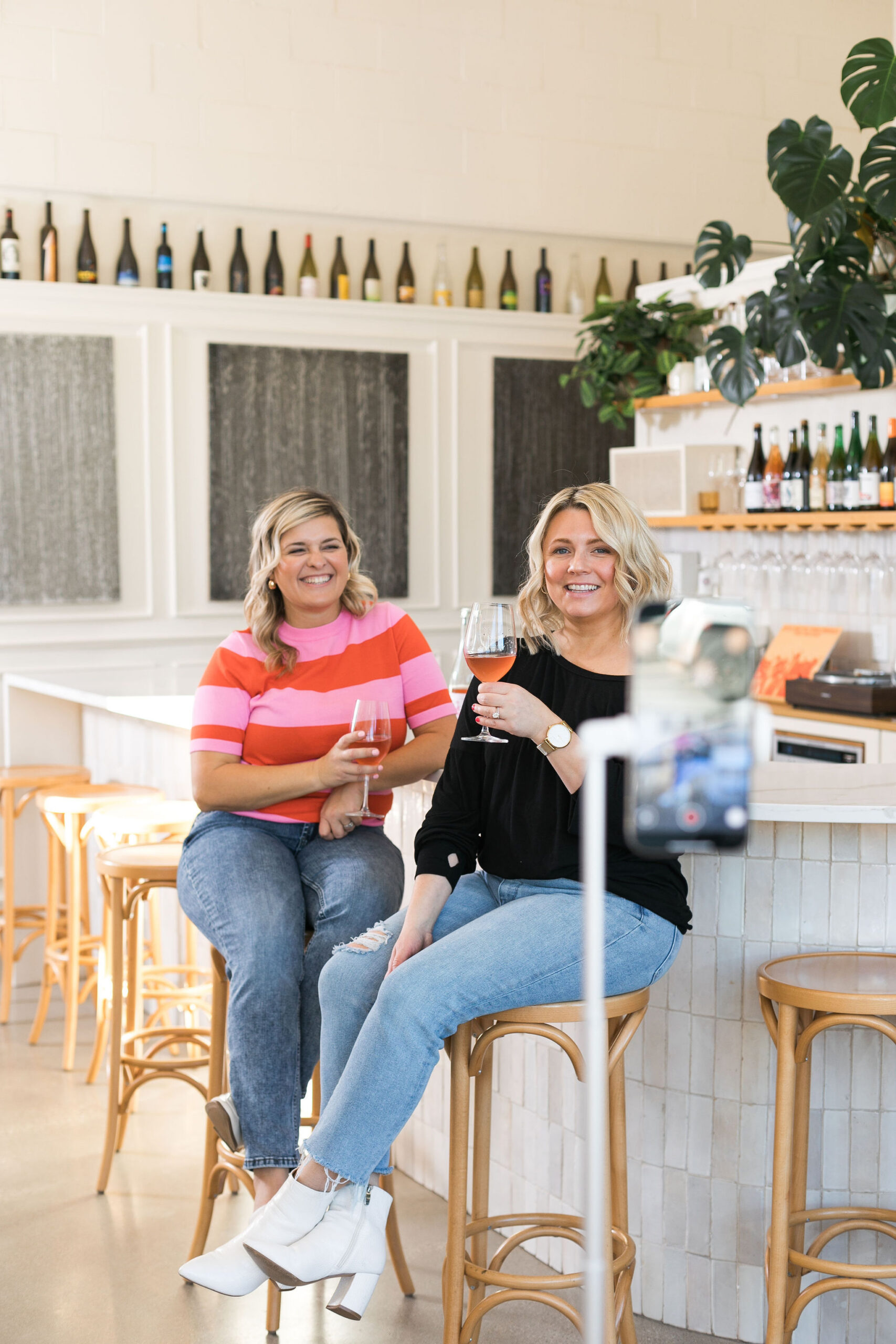 Chelsea and Kayla sitting in a wine bar with a phone on a tripod taking a picture