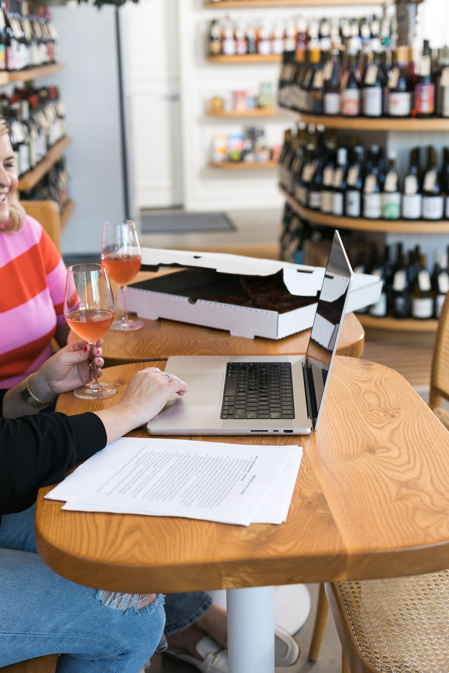 Chelsea and Kayla in front of a laptop holding wine glasses
