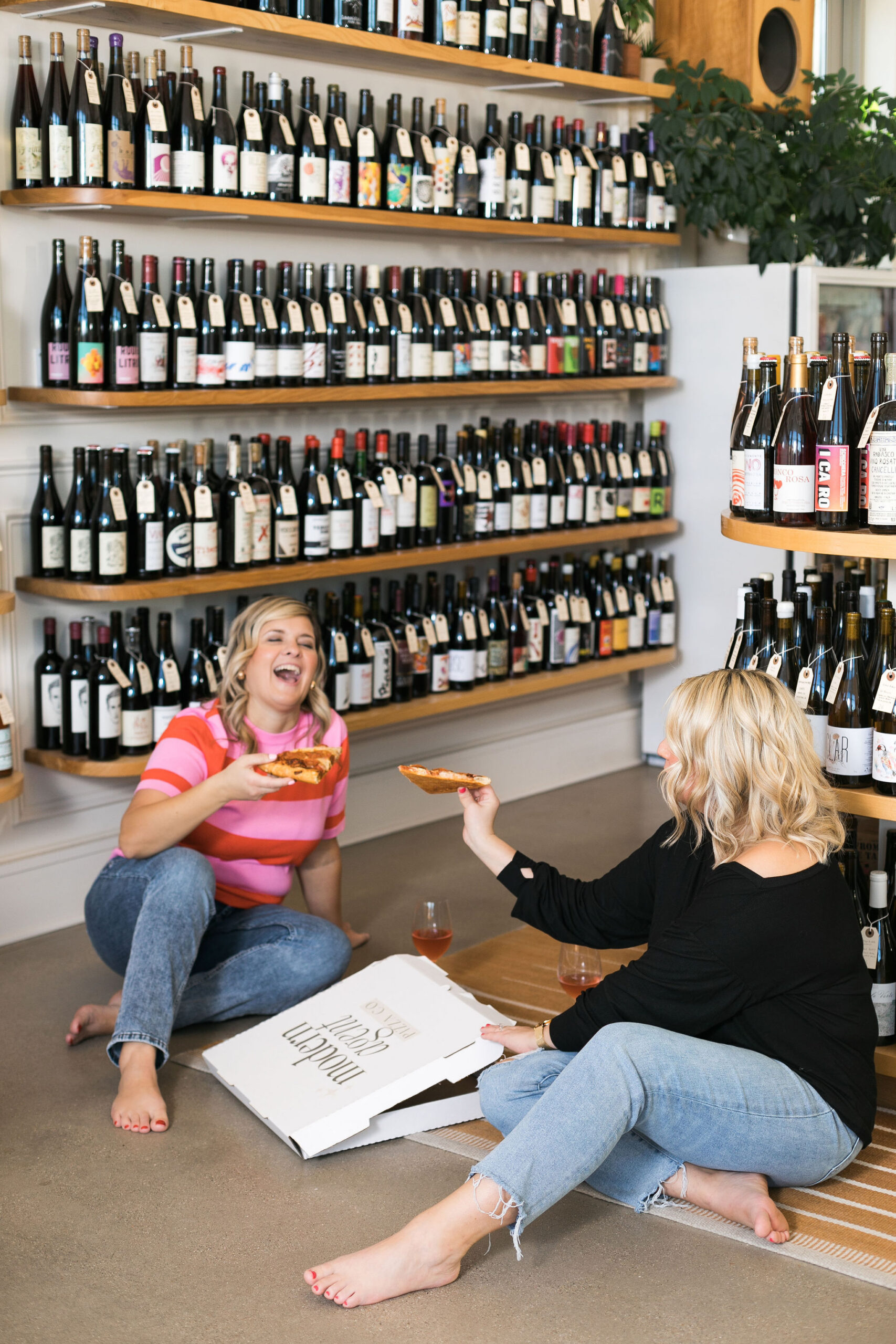 Chelsea and Kayla sitting on the floor eating pizza and laughing